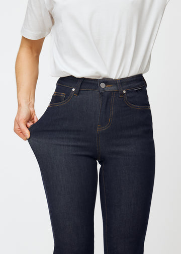 Modellen sträcker djupt mörkblå denim jeans för kvinnor i färgen Midnights vid låret för att visa materialets stretch.
