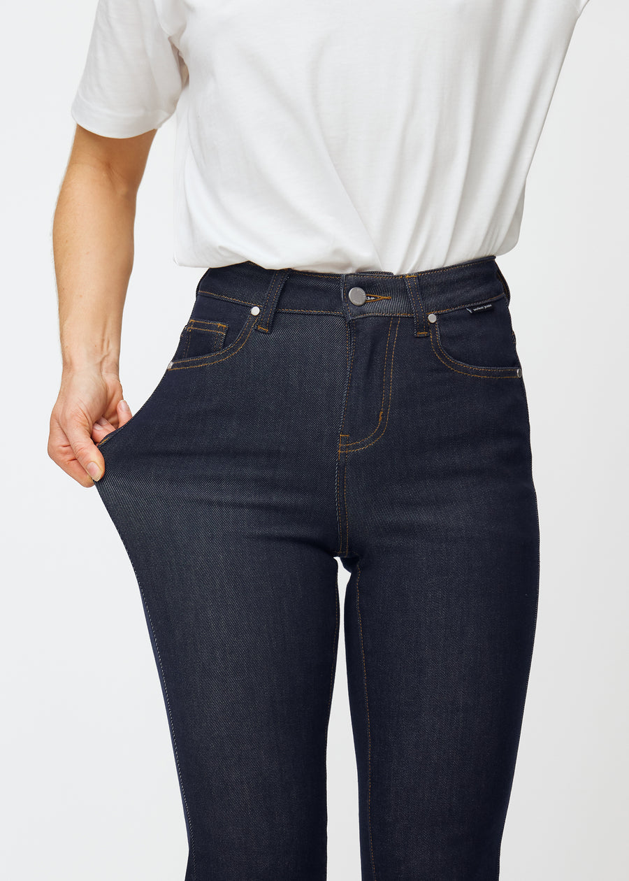 Modellen sträcker djupt mörkblå denim jeans för kvinnor i färgen Midnights vid låret för att visa materialets stretch.
