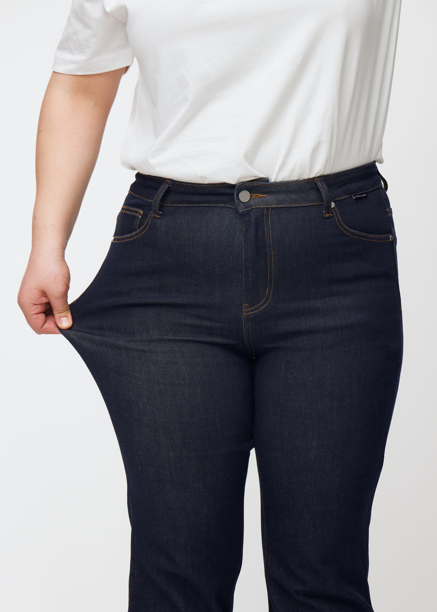 Plus size-modell sträcker djupt mörkblå denim jeans för kvinnor i färgen Midnights vid låret för att visa materialets stretch.