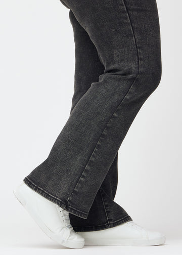 Mörkgrå mid-rise bootcutjeans i färgen Shadows. Närbild vid ankeln på en plus size-modell som visar den lätta utsvängningen nedtill.