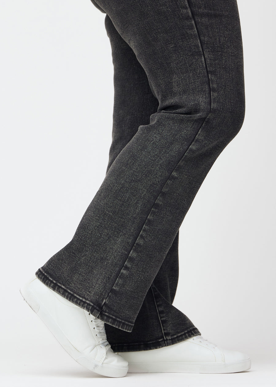 Mörkgrå mid-rise bootcutjeans i färgen Shadows. Närbild vid ankeln på en plus size-modell som visar den lätta utsvängningen nedtill.
