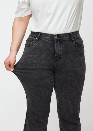 Mörkgrå mid-rise bootcutjeans i färgen Shadows. En plus size-modell drar i jeanstyget vid låret för att visa stretchen.
