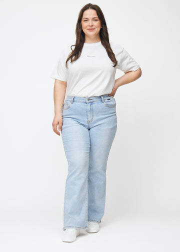 Ljusblå mid-rise bootcutjeans i färgen Waves. Helbild av en plus size-modell i jeansen.