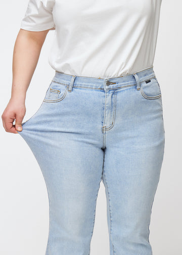 Ljusblå mid-rise bootcutjeans i färgen Waves. En plus size-modell drar i jeanstyget vid låret för att visa stretchen.