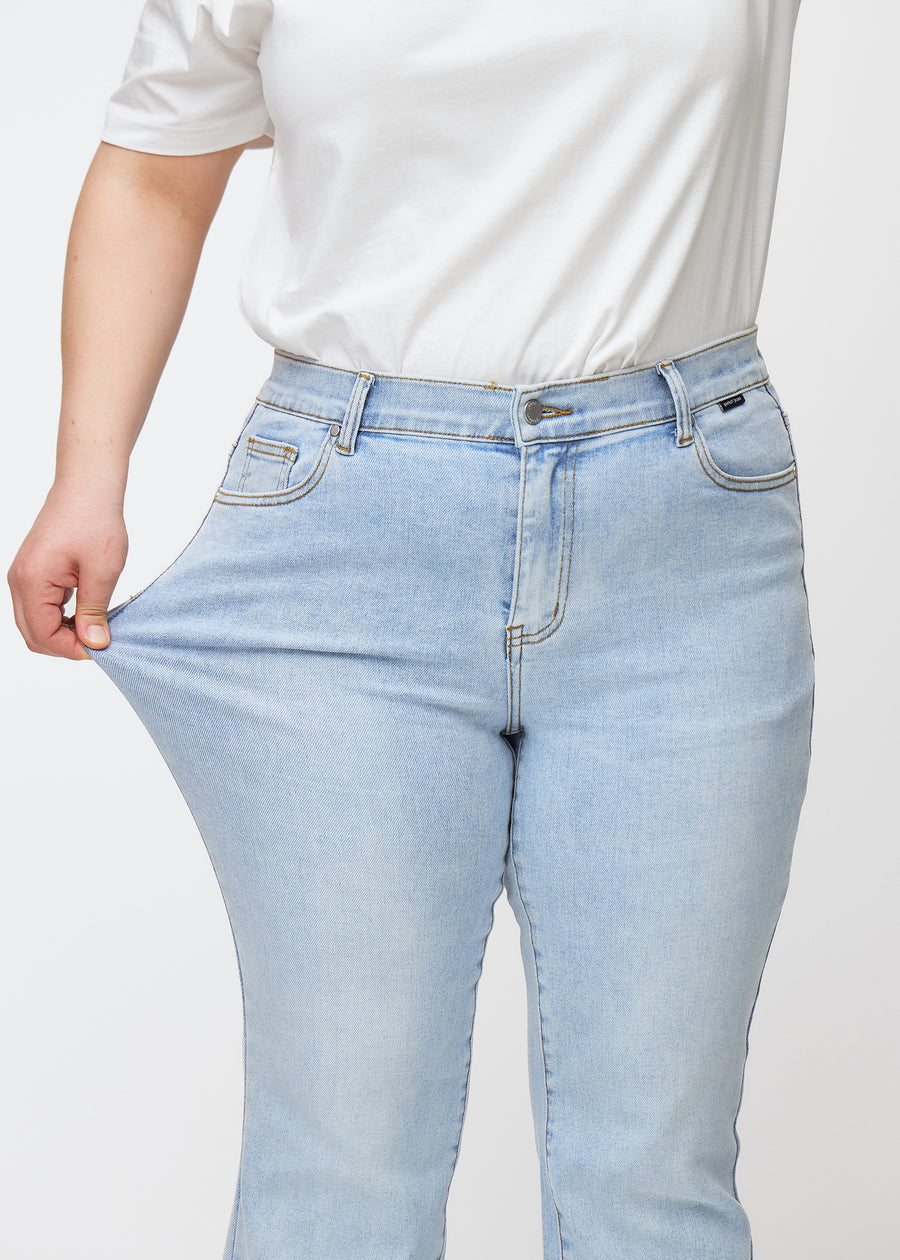 Ljusblå mid-rise bootcutjeans i färgen Waves. En plus size-modell drar i jeanstyget vid låret för att visa stretchen.
