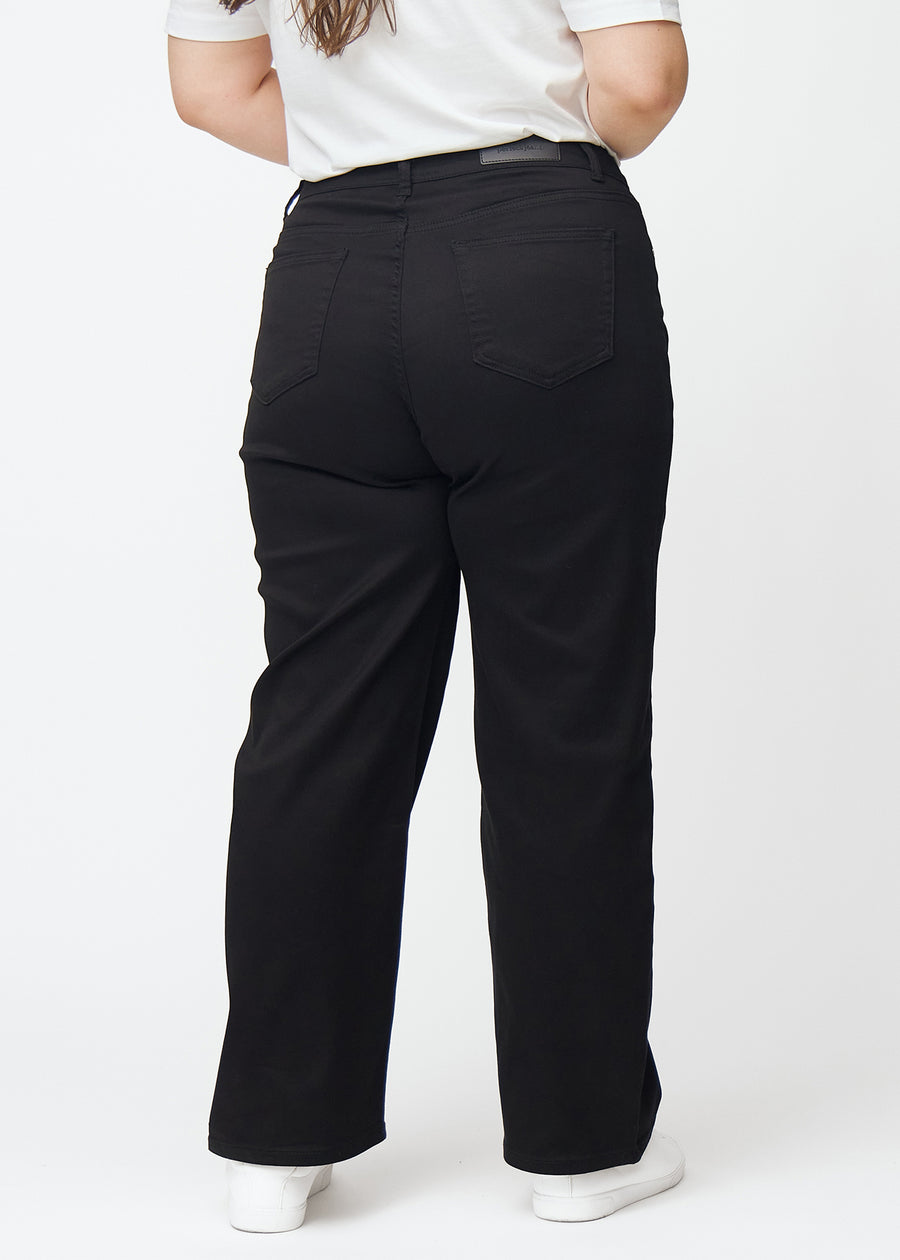 Svarta högmidjade jeans, som sitter åt i midjan och har en lös passform med vidd nedtill, sedda bakifrån på en plus-size-modell så att man kan se hela produkten.