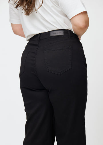 Svarta högmidjade jeans, som sitter åt i midjan och har en lös passform med vidd nedtill, sedda nära bakifrån på en plus-size-modell för att visa detaljer.