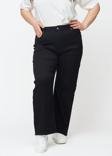 Svarta högmidjade jeans i modellen Ravens, som sitter åt i midjan och har en lös passform med vidd nedtill, på en plus-size-modell sedd framifrån.
