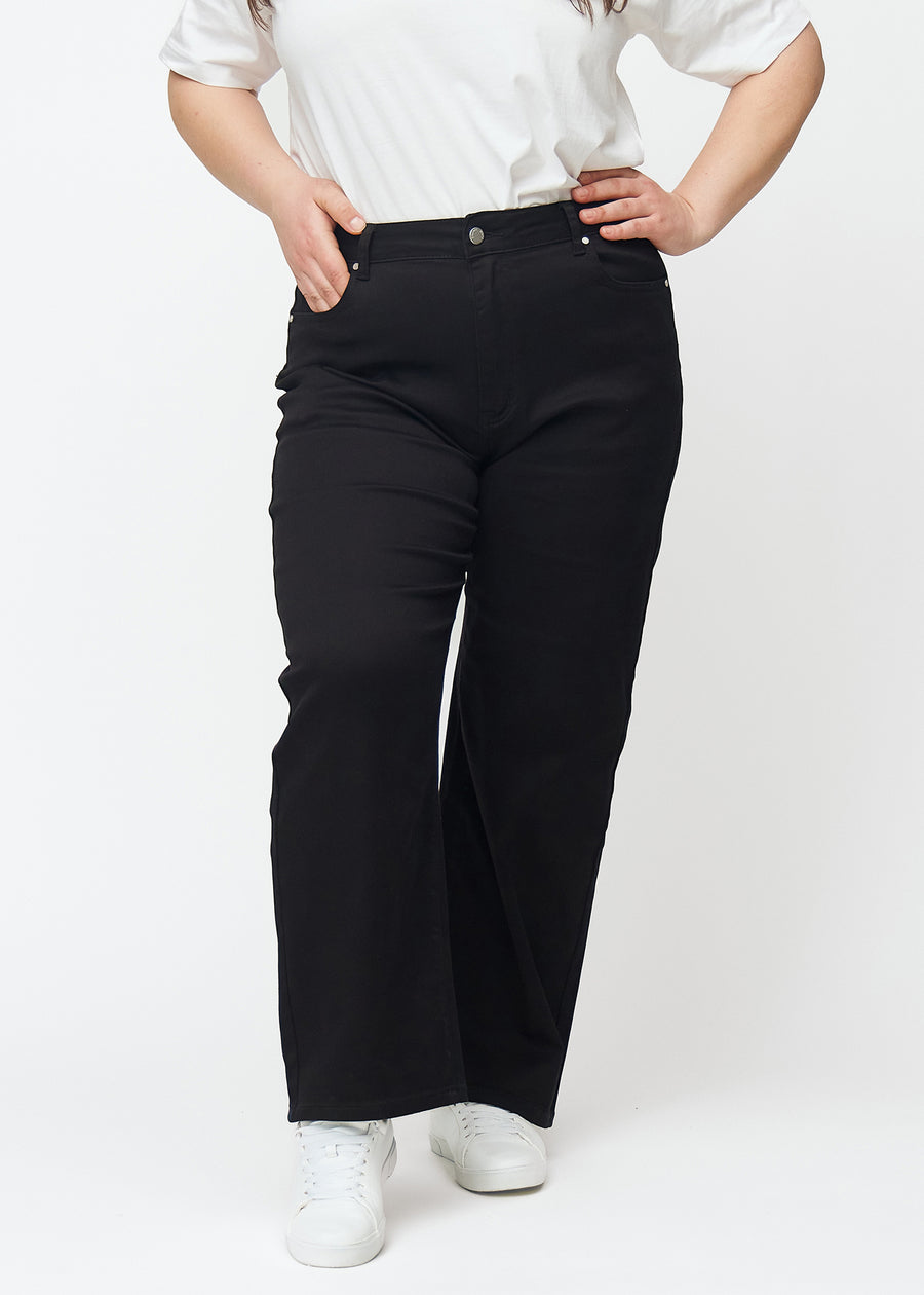 Svarta högmidjade jeans i modellen Ravens, som sitter åt i midjan och har en lös passform med vidd nedtill, på en plus-size-modell sedd framifrån.