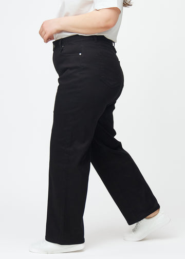 Svarta högmidjade jeans, som sitter åt i midjan och har en lös passform med vidd nedtill, sedda från sidan på en plus-size-modell.