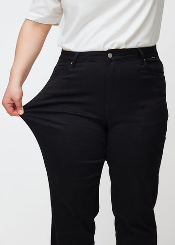 Plus-size-modellen sträcker ut jeansen vid låret för att visa stretch.