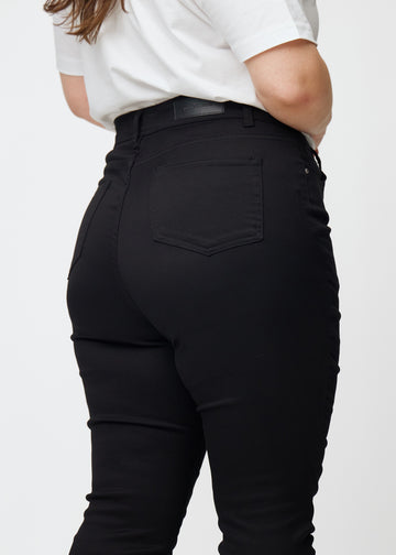 Bilden visar en närbild av svarta plus size high rise jeans för kvinnor i färgen Ravens i skinny fit sedda bakifrån.