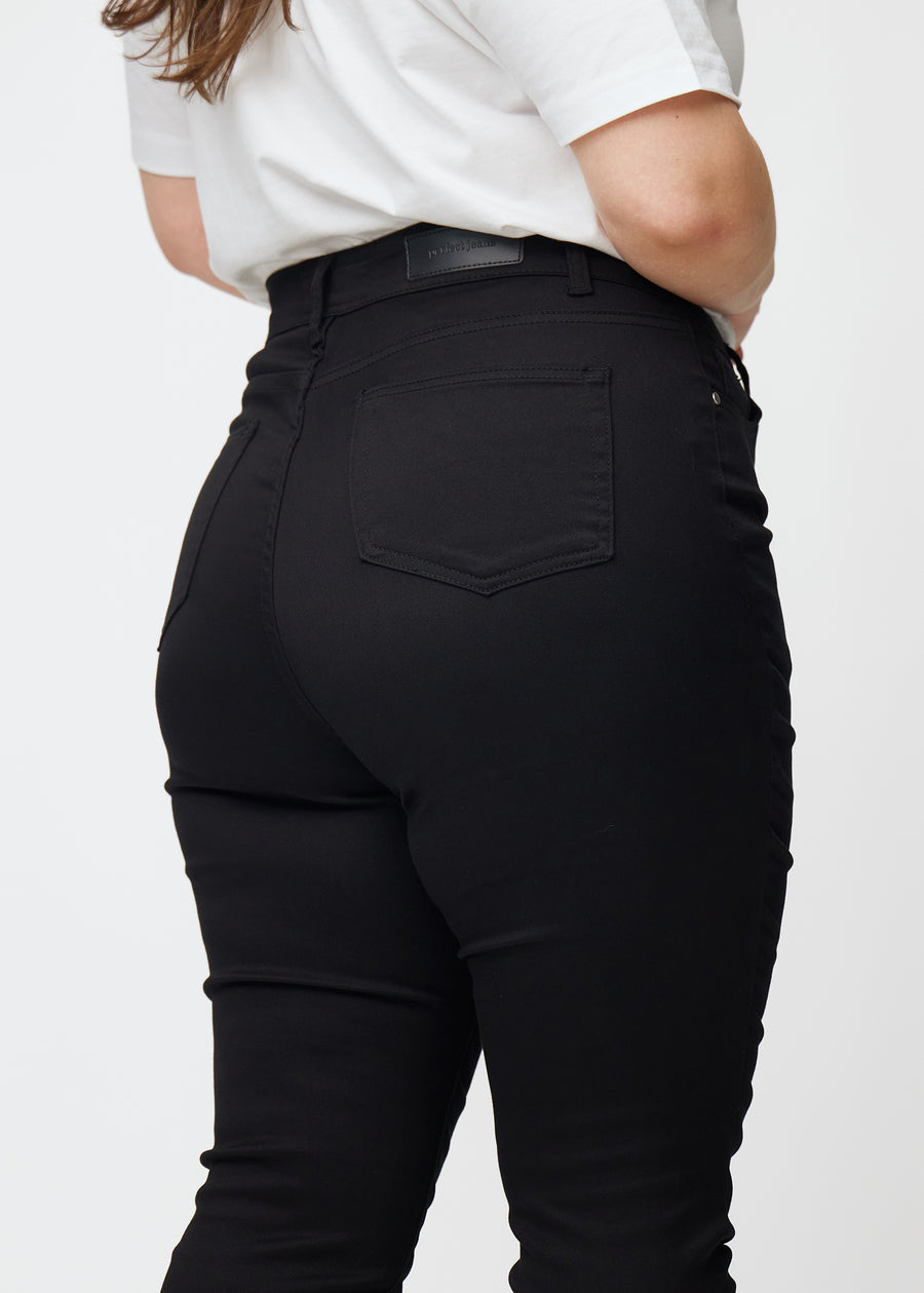 Bilden visar en närbild av svarta plus size high rise jeans för kvinnor i färgen Ravens i skinny fit sedda bakifrån.