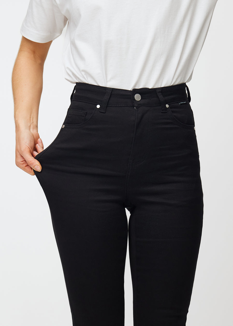 En modell sträcker de svarta Ravens stretch jeans med hög midja för att illustrera passformen.