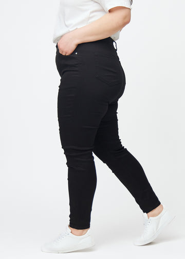 Svarta plus size high rise skinny jeans för kvinnor i färgen Ravens ses från sidan på en modell.