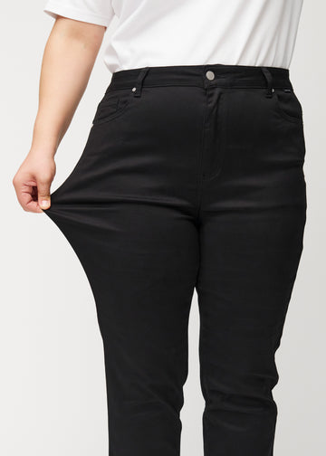 Plus-size-modellen sträcker ut jeansen vid låret för att visa stretch.