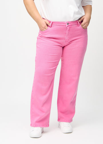 Ljusrosa loose jeans, modellnamn Flamingos, som sitter löst med mycket vidd i benen på en plus size-modell, sedd framifrån.