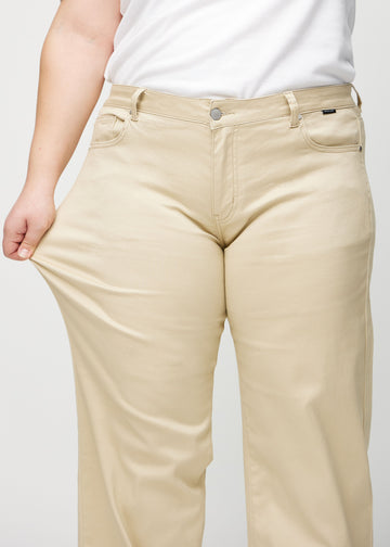 Loose jeans för kvinnor i beige, färgen Gazelles. En plus size-modell drar i jeanstyget vid låret för att visa stretchen.