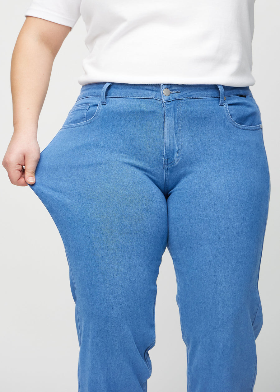 Loose jeans för kvinnor i blå, färgen Geraniums. En plus size-modell drar i jeanstyget vid låret för att visa stretchen.