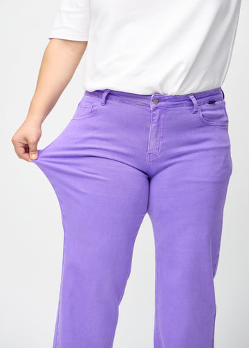 Loose jeans för kvinnor i lila, färgen Lavenders. En plus size-modell drar i jeanstyget vid låret för att visa stretchen.