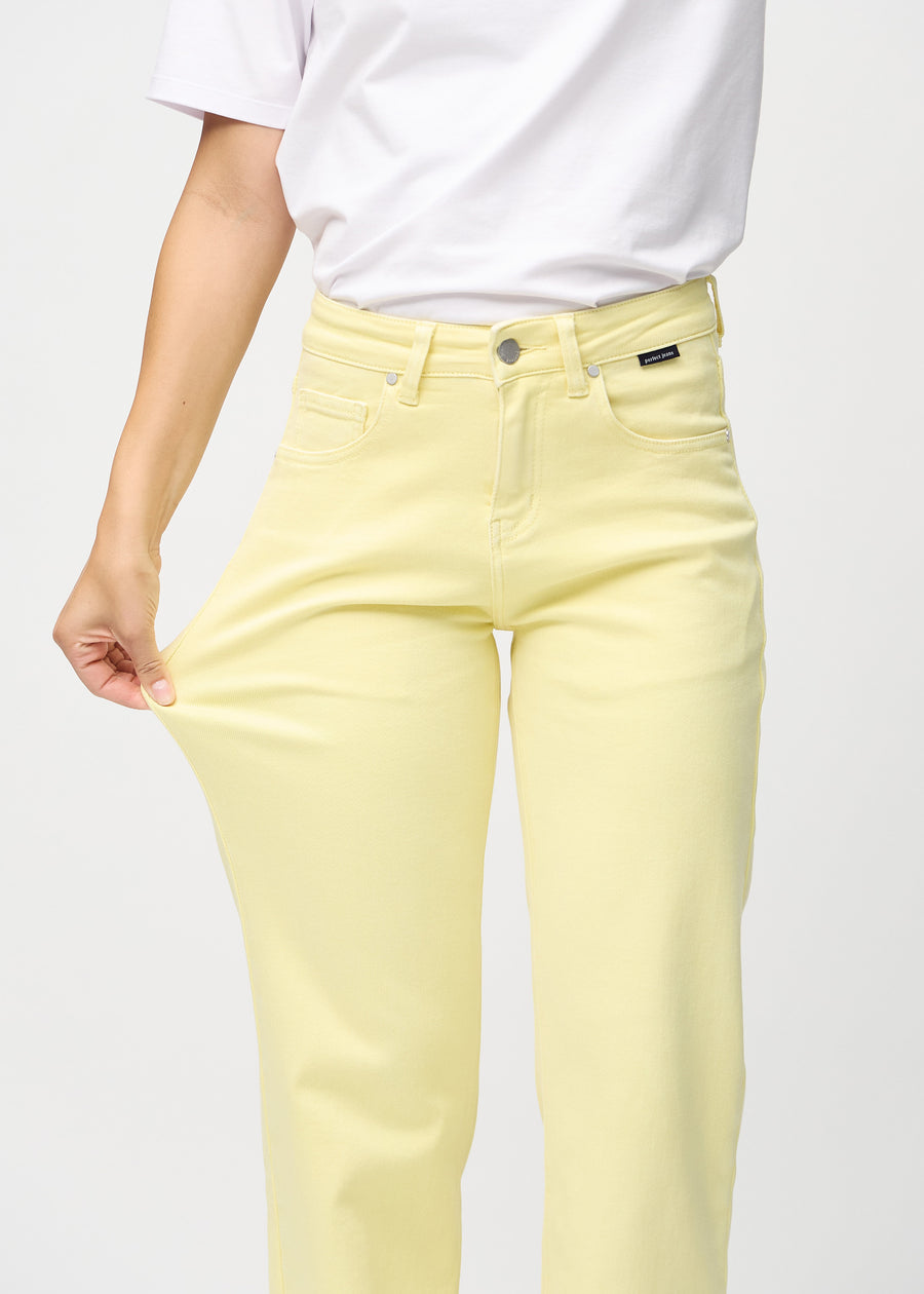 Loose jeans för kvinnor i ljusgul, färgen Lemonades. En modell drar i jeanstyget vid låret för att visa stretchen.
