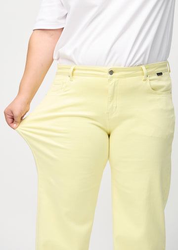 Loose jeans för kvinnor i ljusgul, färgen Lemonades. En plus size-modell drar i jeanstyget vid låret för att visa stretchen.