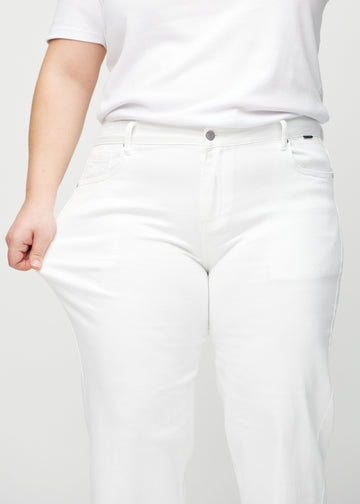 Loose jeans för kvinnor i vit, färgen Marguerites. En plus size-modell drar i jeanstyget vid låret för att visa stretchen.