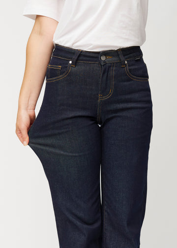 Modellen sträcker den djupa mörkblå denimen jeans för kvinnor i färgen Midnights vid låret för att visa materialets stretch.