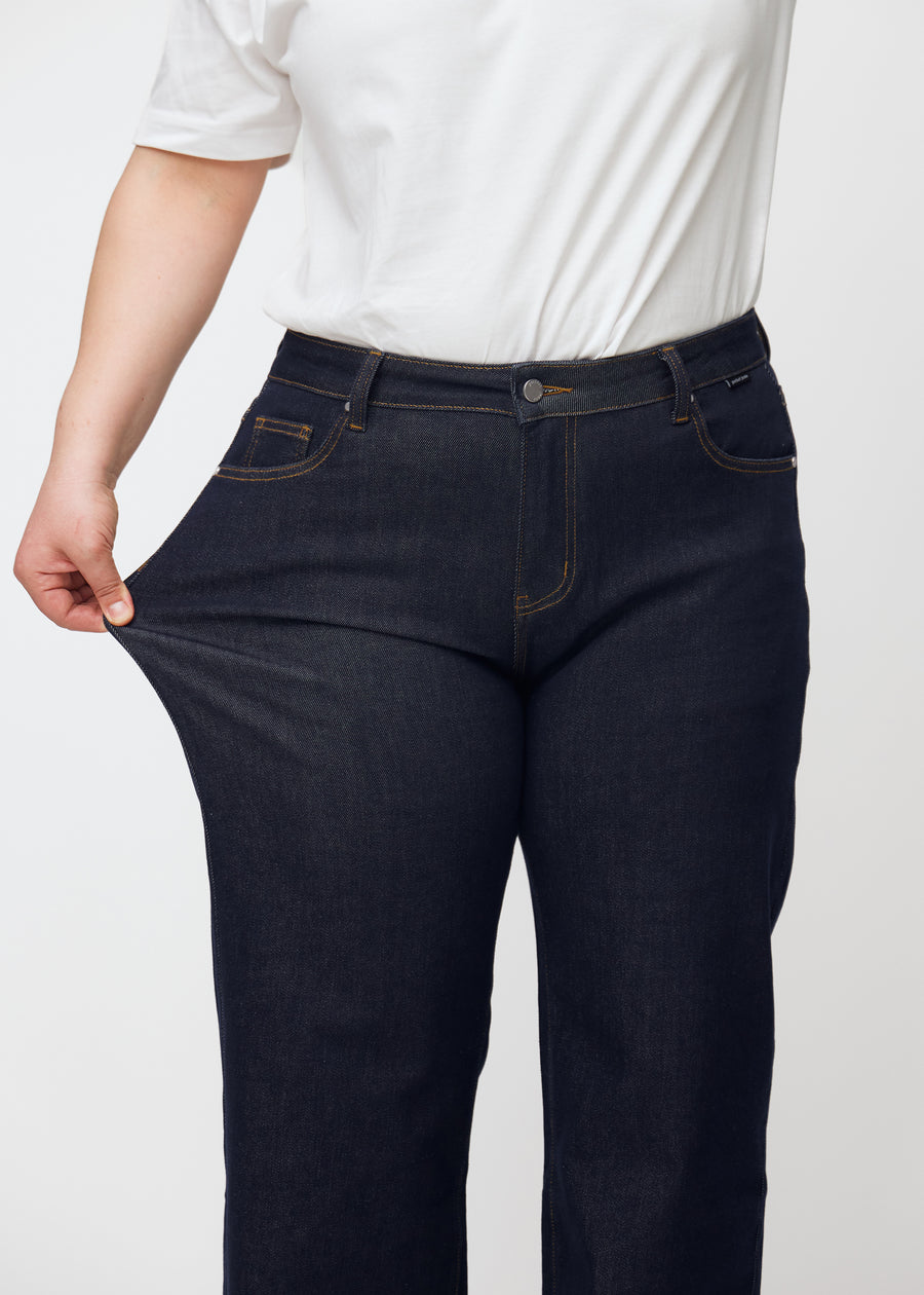 Plus-size-modell sträcker den djupt mörkblå denim jeans för kvinnor i färgen Midnights vid låret för att visa materialets stretch.