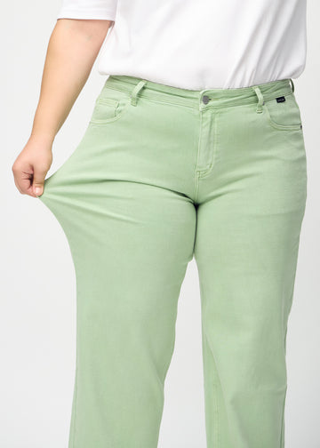 Loose jeans för kvinnor i ljusgrön, färgen Mints. En plus size-modell drar i jeanstyget vid låret för att visa stretchen.