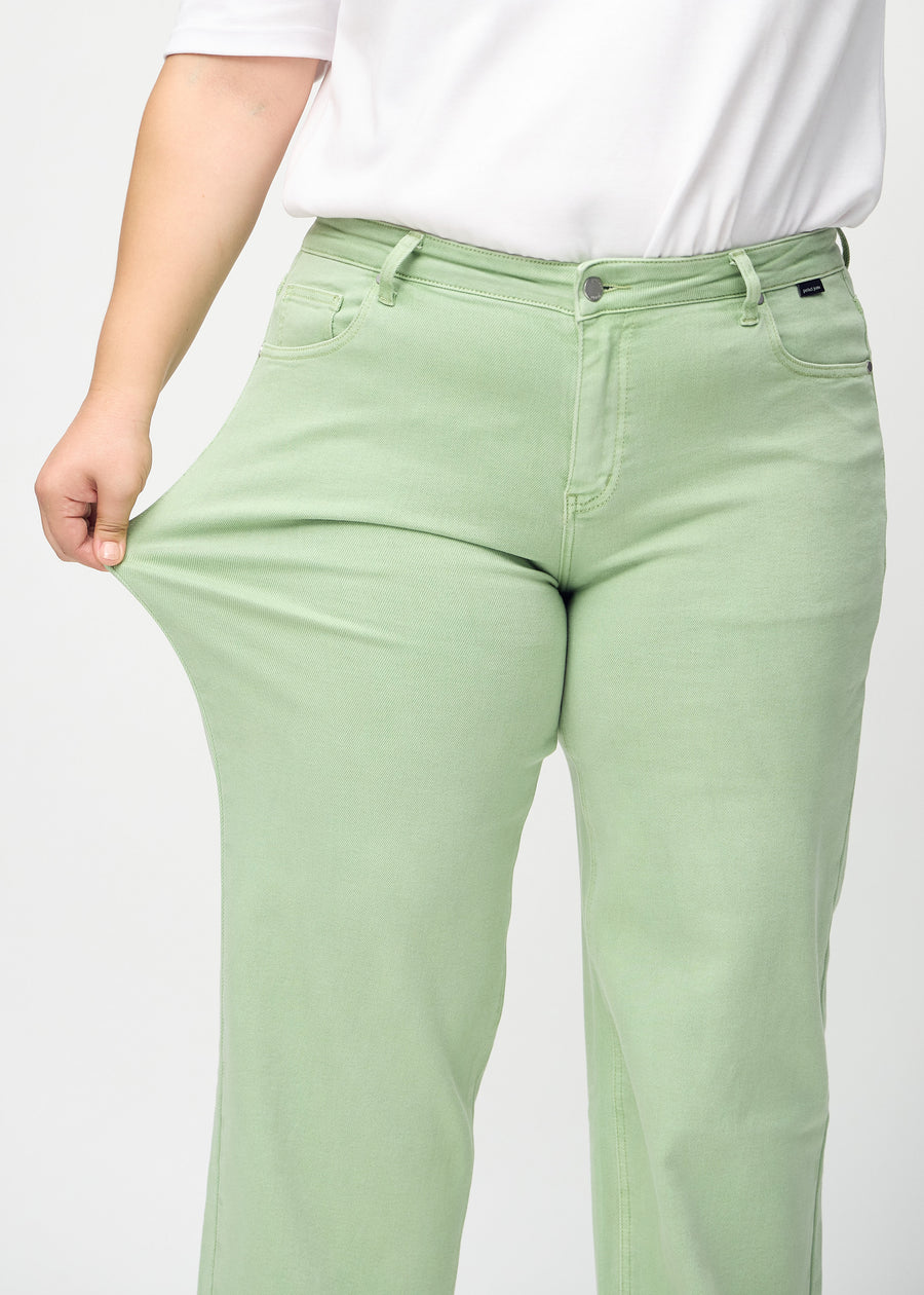 Loose jeans för kvinnor i ljusgrön, färgen Mints. En plus size-modell drar i jeanstyget vid låret för att visa stretchen.