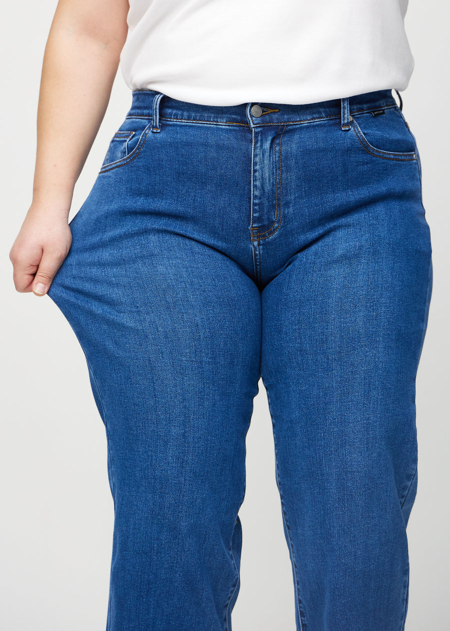 Loose jeans för kvinnor i mörkblå, färgen Oceans. En plus size-modell drar i jeanstyget vid låret för att visa stretchen.