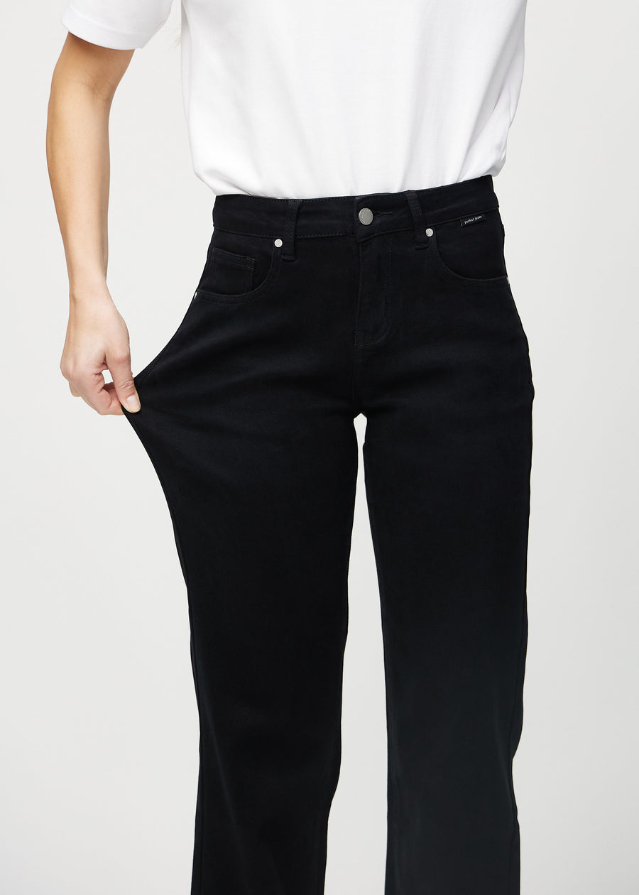 Loose jeans för kvinnor i svart, färgen Ravens. En modell drar i jeanstyget vid låret för att visa stretchen.