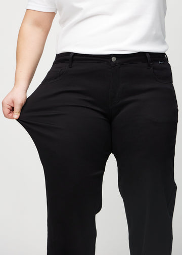 Loose jeans för kvinnor i svart, färgen Ravens. En plus size-modell drar i jeanstyget vid låret för att visa stretchen.