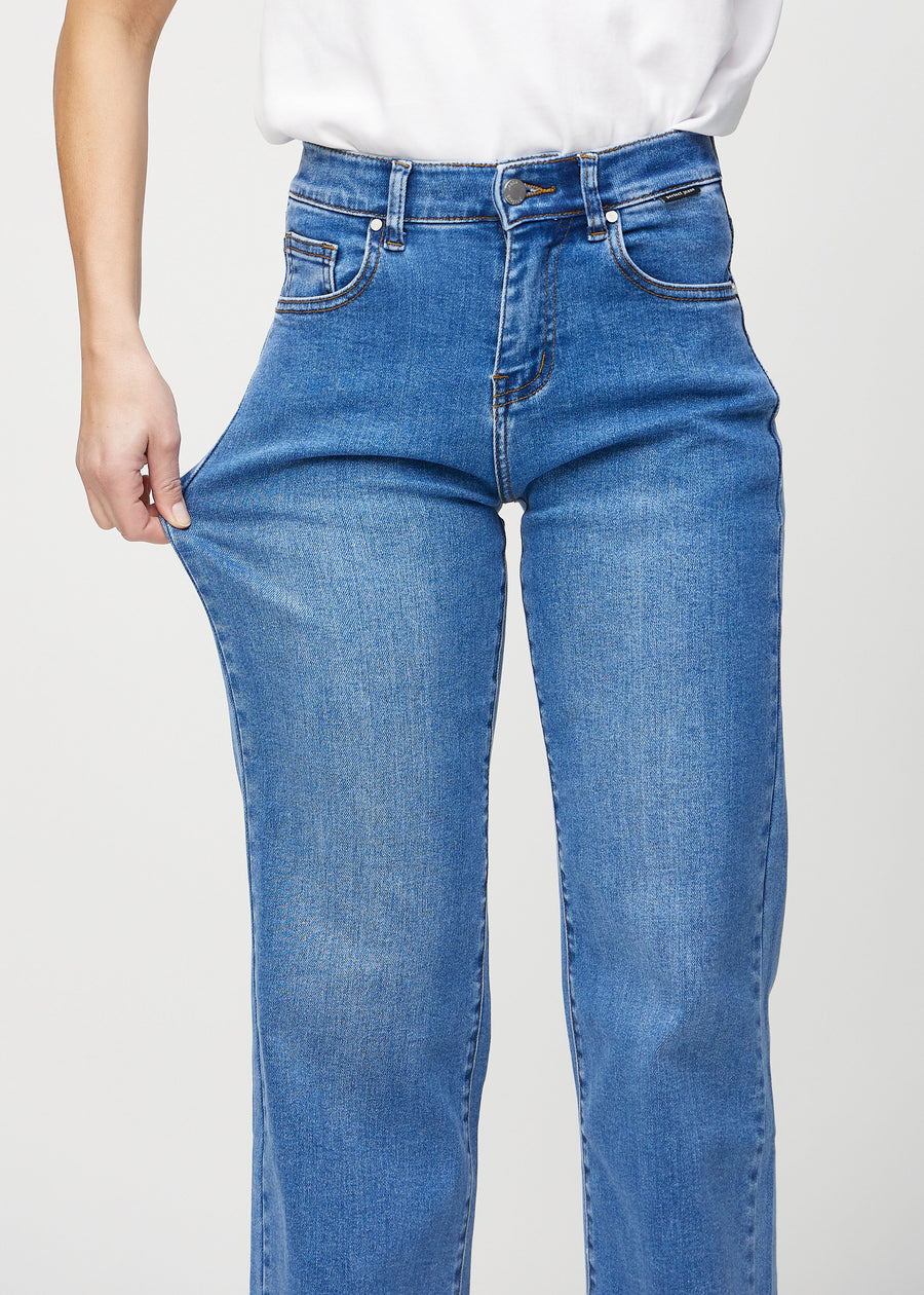 Loose jeans för kvinnor i blå, färgen Rivers. En modell drar i jeanstyget vid låret för att visa stretchen.