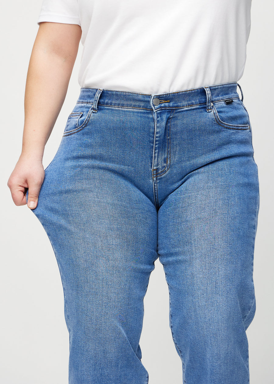 Loose jeans för kvinnor i blå, färgen Rivers. En plus size-modell drar i jeanstyget vid låret för att visa stretchen.