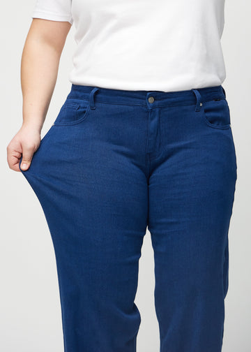 Loose jeans för kvinnor i mörkblå, färgen Royals. En plus size-modell drar i jeanstyget vid låret för att visa stretchen.