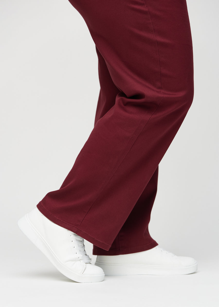 Loose jeans för kvinnor i mörkröd, färgen Santas. Närbild vid anklarna på en plus size-modell, som visar de vida bensluten.