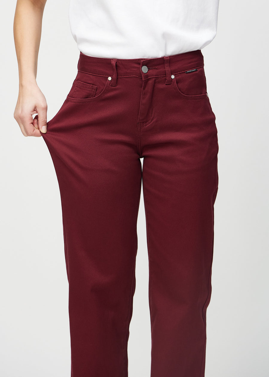 Loose jeans för kvinnor i mörkröd, färgen Santas. En modell drar i jeanstyget vid låret för att visa stretchen.