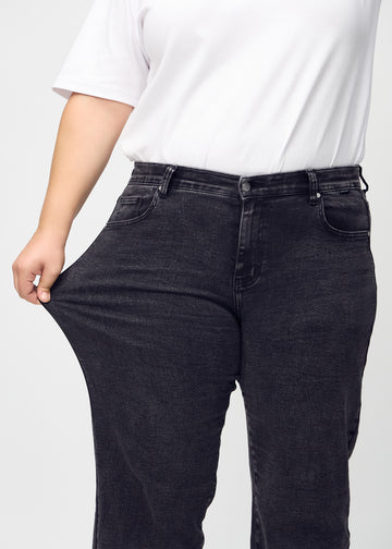 Plus-size-modellen sträcker jeansen vid låret för att visa stretch.