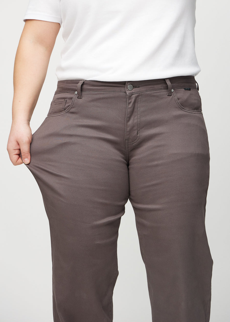 Loose jeans för kvinnor i gråbrun, färgen Thunders. En plus size-modell drar i jeanstyget vid låret för att visa stretchen.