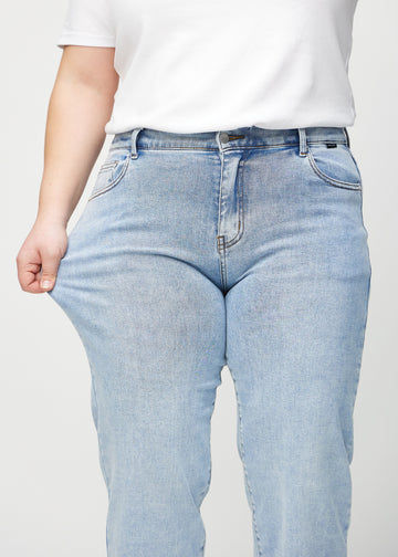 Plus-size-modellen sträcker jeansen vid låret för att visa stretch.