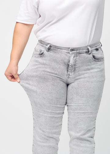 Regularjeans för kvinnor i ljusgrå, färgen Ashes. En plus size-modell drar i tyget vid låret för att visa stretchen.