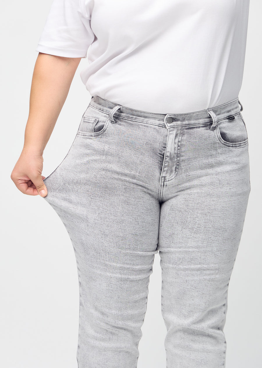 Regularjeans för kvinnor i ljusgrå, färgen Ashes. En plus size-modell drar i tyget vid låret för att visa stretchen.