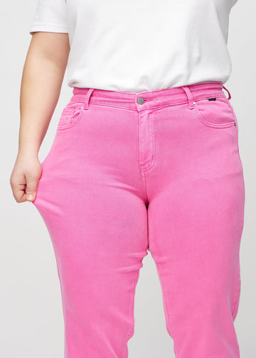 Regularjeans för kvinnor i ljusrosa, färgen Flamingos. En plus size-modell drar i tyget vid låret för att visa stretchen.