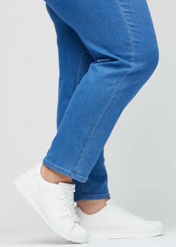 Regularjeans för kvinnor i blå, färgen Geraniums. Närbild vid anklarna på en plus size-modell, som visar de raka bensluten.