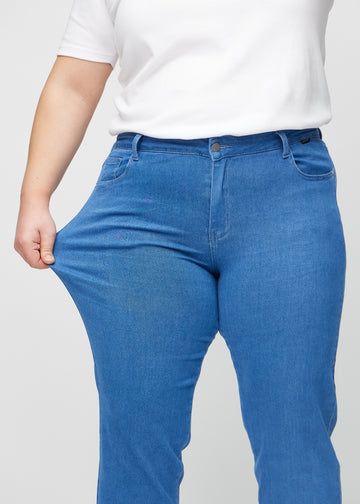 Regularjeans för kvinnor i blå, färgen Geraniums. En plus size-modell drar i tyget vid låret för att visa stretchen.