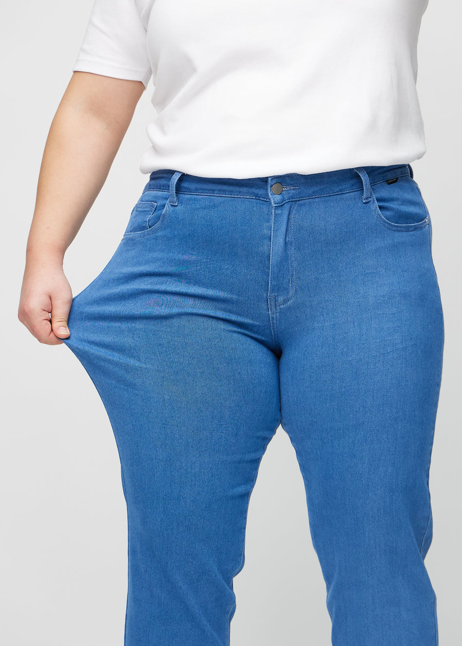 Regularjeans för kvinnor i blå, färgen Geraniums. En plus size-modell drar i tyget vid låret för att visa stretchen.