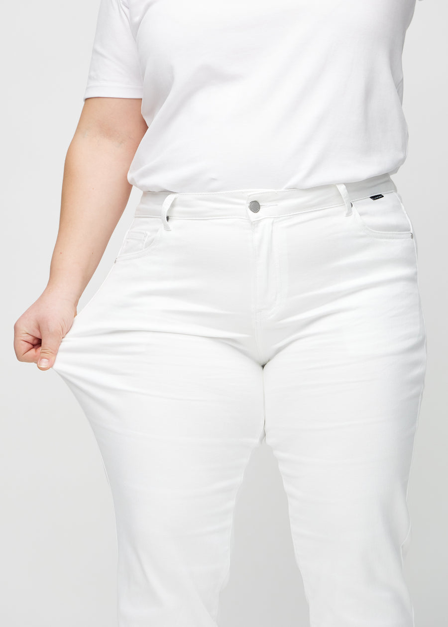 Regularjeans för kvinnor i vit, färgen Marguerites. En plus size-modell drar i tyget vid låret för att visa stretchen.