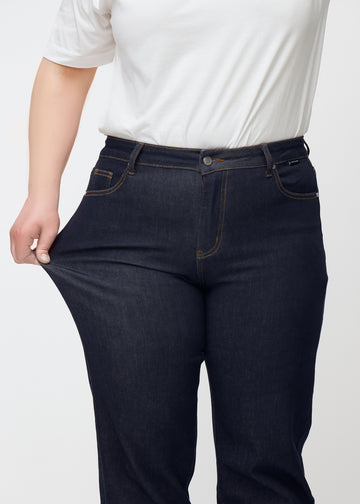 Plus size-modell sträcker den djupt mörkblå denimen jeans för kvinnor i färgen Midnights vid låret för att visa materialets stretch.